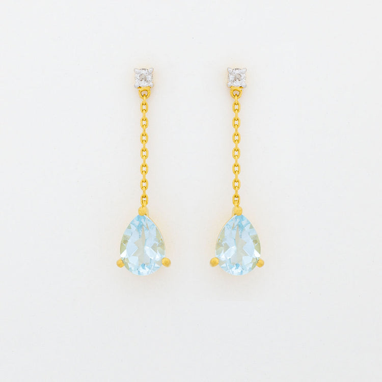 A pair of dangle earrings featuring a small white topaz gemstone at the top and a pear cut blue topaz gemstone at the bottom, attached to a gold-colored chain.