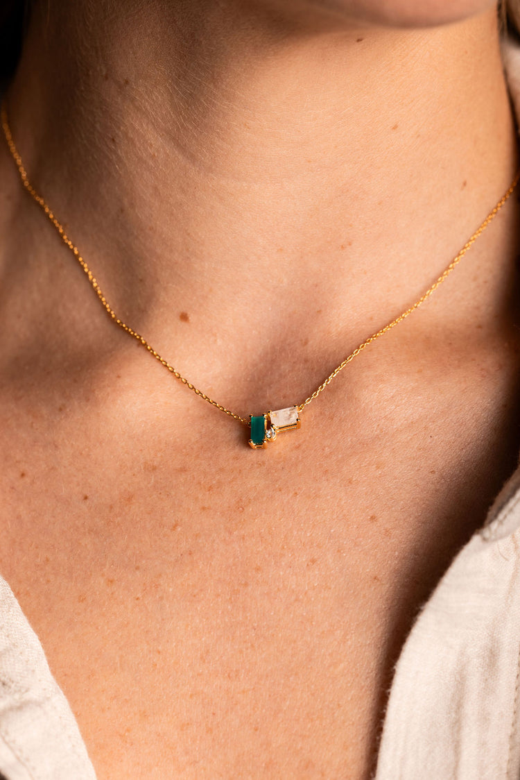 A person wearing a gold-colored necklace with a green onyx and moonstone cluster.
