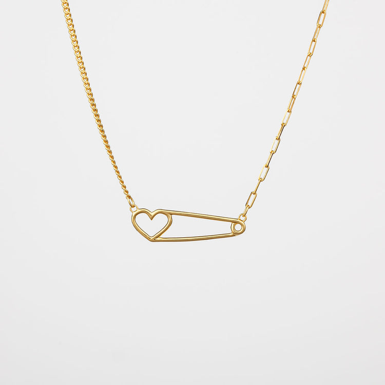 A gold-colored heart pin necklace with a curb chain on one side and a paperclip chain on the other side
