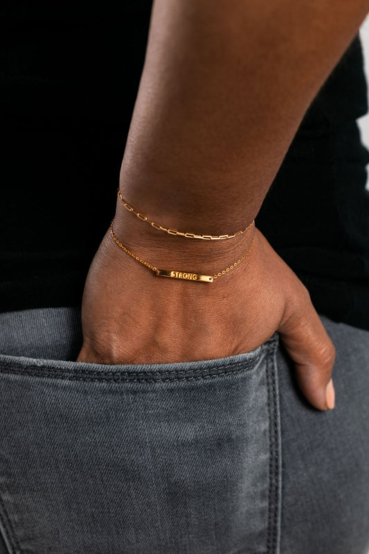 A person wearing a gold-colored bracelet with the word 'STRONG' written on it