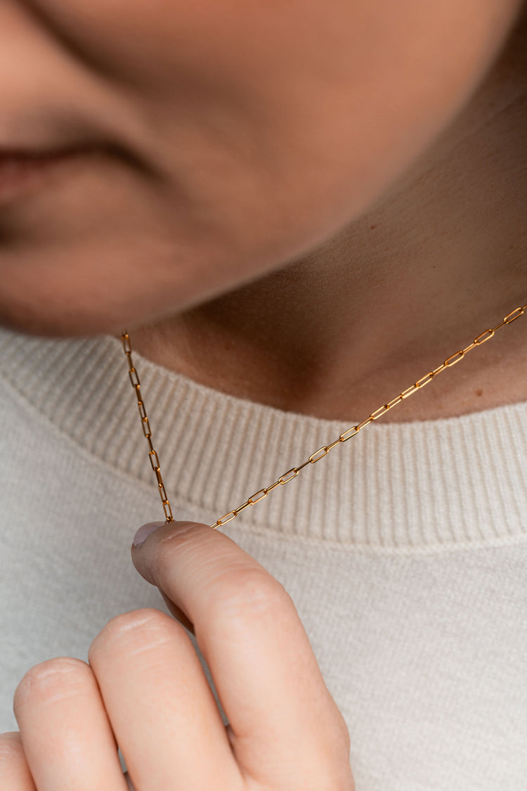 Close-up of a person wearing a gold necklace with a neutral background