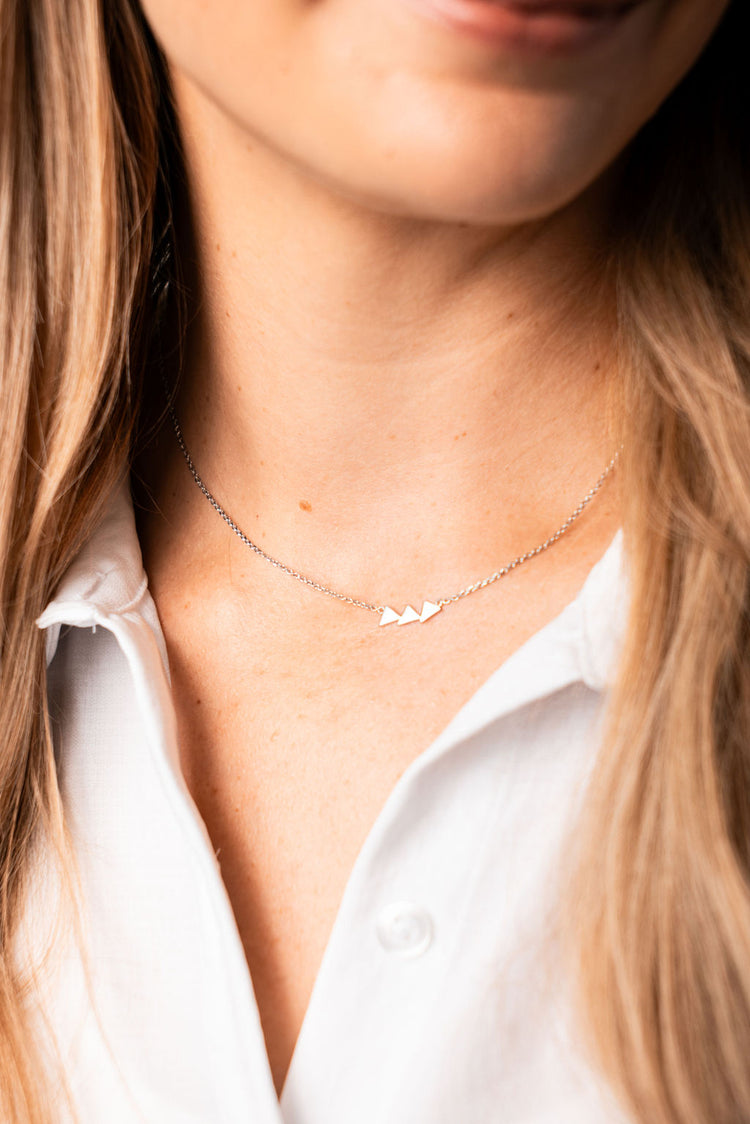 silver triangle necklace on a silver chain on a woman with blonde hair wearing a white shirt