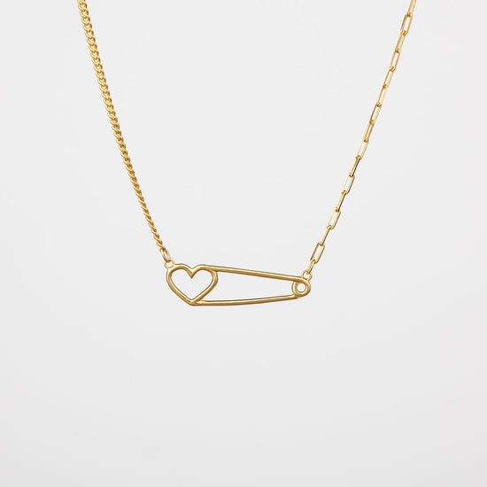 A gold-colored heart pin necklace with a curb chain on one side and a paperclip chain on the other side