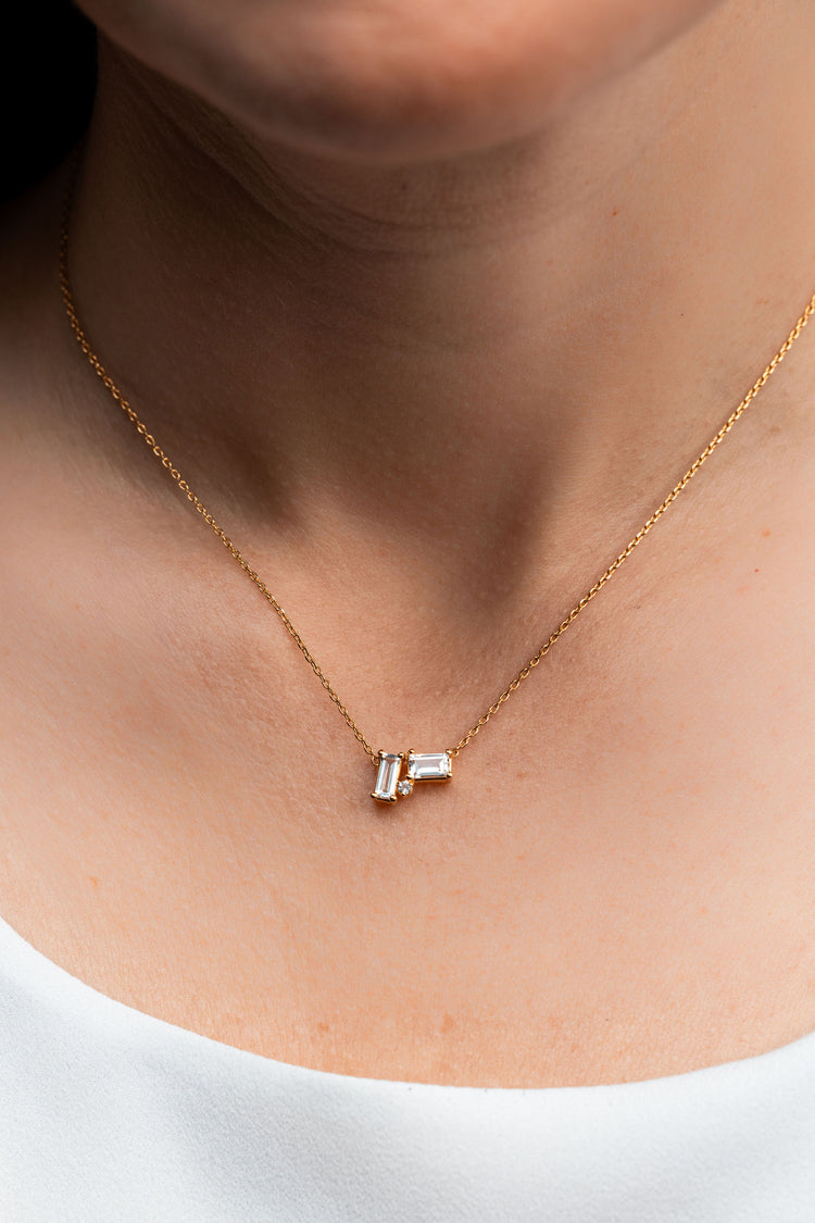Gold necklace with a small pendant on a person wearing a white top.